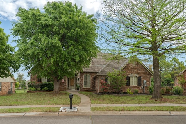 view of front of property featuring roof with shingles, brick siding, and a front yard