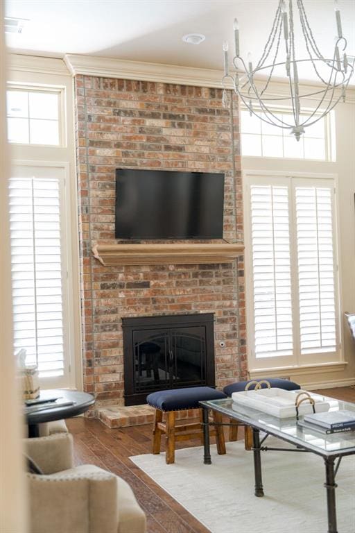 living room featuring crown molding, a brick fireplace, a chandelier, and hardwood / wood-style floors