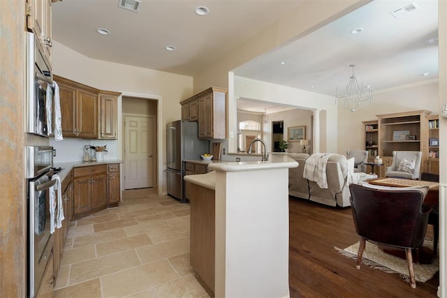 kitchen with appliances with stainless steel finishes, a chandelier, a peninsula, open floor plan, and visible vents
