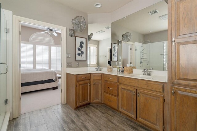 ensuite bathroom featuring visible vents, double vanity, wood finished floors, a sink, and a stall shower