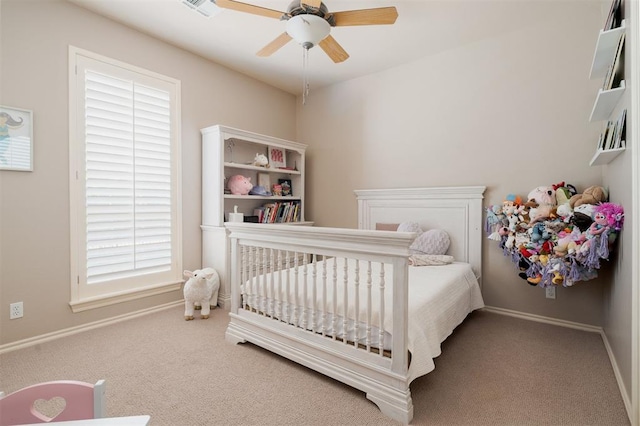 carpeted bedroom with a crib, baseboards, ceiling fan, and visible vents