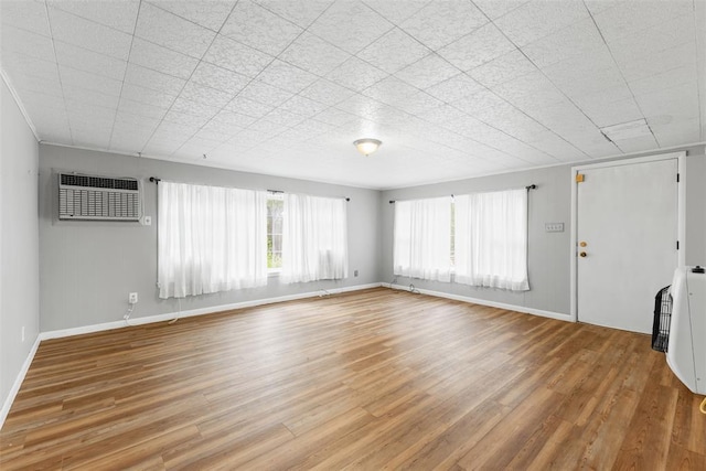 1201 E 18th St, Ada, OK 74820 - unfurnished living room featuring baseboards, a wall mounted AC, and light wood-style flooring