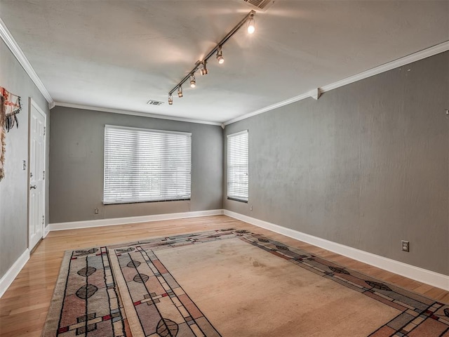 empty room featuring track lighting, visible vents, ornamental molding, and wood finished floors