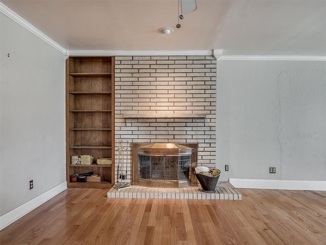 interior space featuring crown molding, baseboards, a brick fireplace, wood finished floors, and built in features