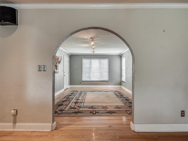 interior space with crown molding, arched walkways, wood finished floors, and baseboards