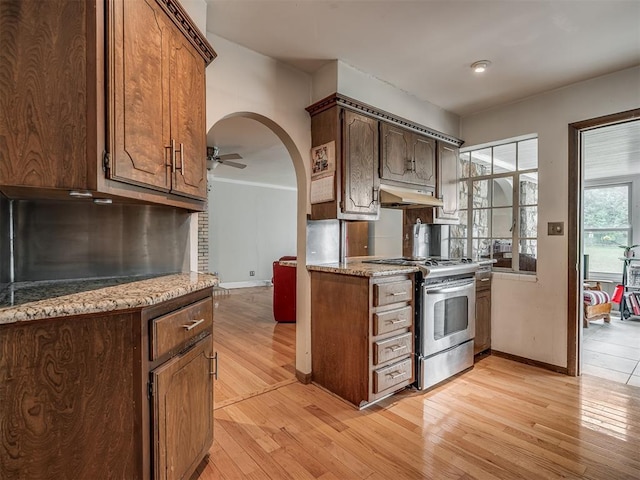 kitchen featuring baseboards, stainless steel gas range oven, light wood-type flooring, and under cabinet range hood