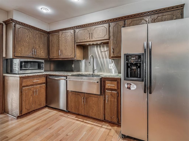 kitchen with stainless steel appliances, light countertops, light wood-style flooring, and a sink