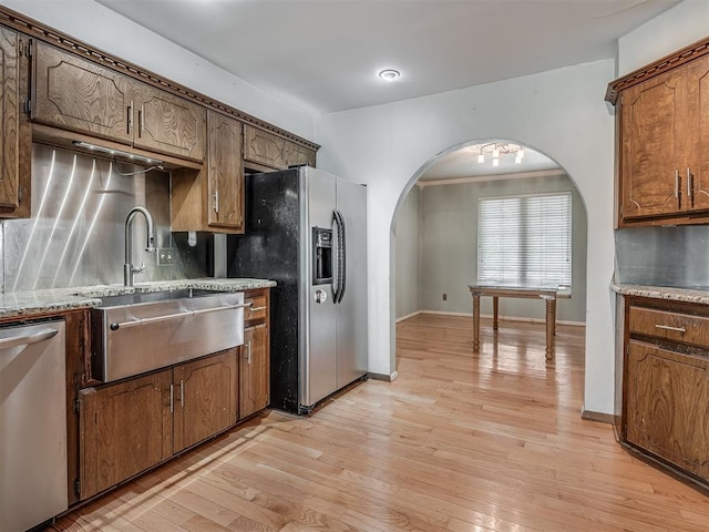 kitchen featuring light wood finished floors, a sink, decorative backsplash, arched walkways, and appliances with stainless steel finishes