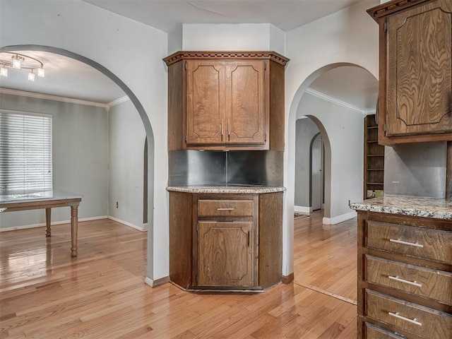 kitchen with light wood-type flooring, ornamental molding, and arched walkways