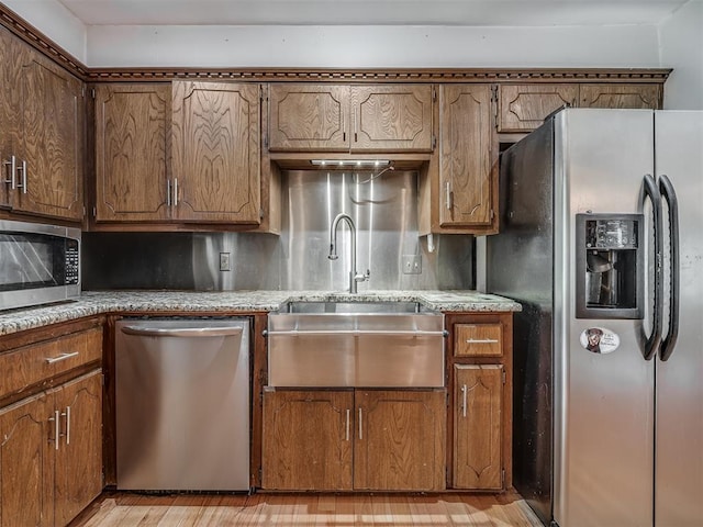 kitchen with a sink, brown cabinetry, light wood-type flooring, light countertops, and appliances with stainless steel finishes
