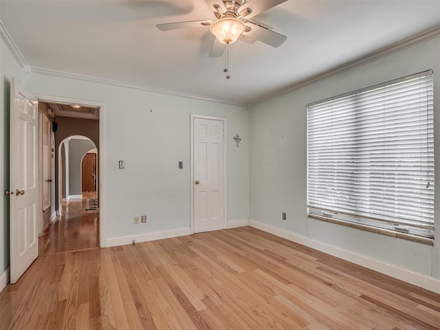 unfurnished room featuring light wood-type flooring, ornamental molding, and arched walkways
