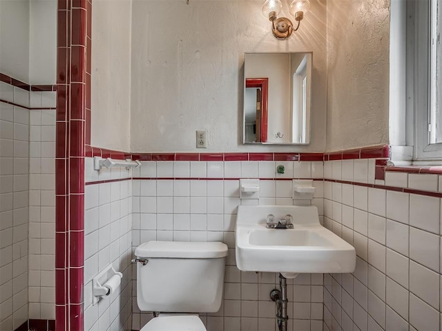 half bathroom featuring a sink, a textured wall, a wainscoted wall, toilet, and tile walls