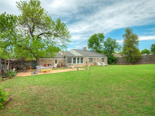 rear view of house with stone siding, a chimney, a patio area, a lawn, and a fenced backyard