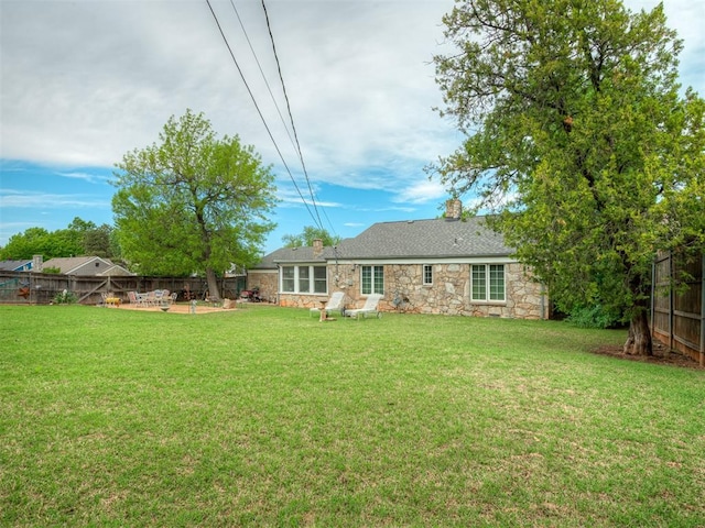 back of house with a chimney, a fenced backyard, a yard, and stone siding