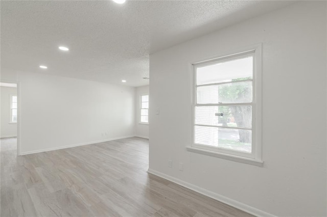 unfurnished room featuring baseboards, light wood-type flooring, a textured ceiling, and recessed lighting