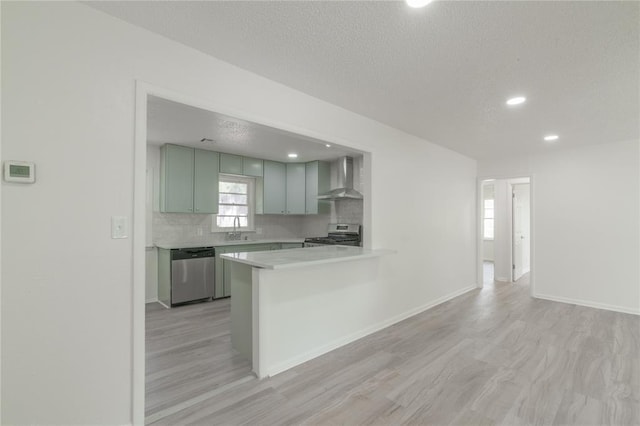kitchen featuring a sink, stainless steel appliances, tasteful backsplash, wall chimney range hood, and light countertops