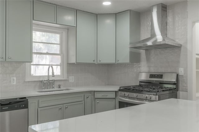 kitchen with a sink, stainless steel appliances, decorative backsplash, wall chimney range hood, and light countertops