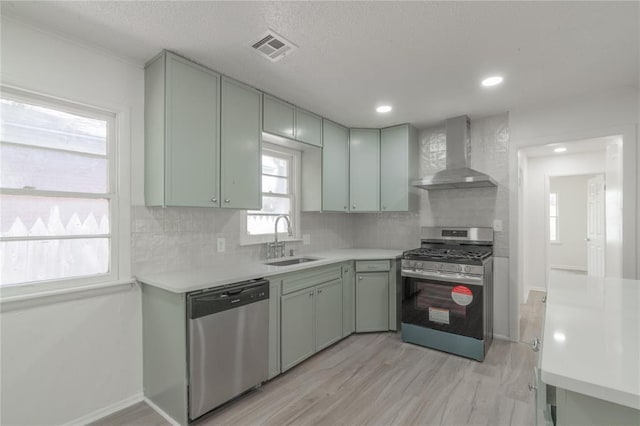 kitchen with wall chimney range hood, a sink, visible vents, stainless steel appliances, and light countertops