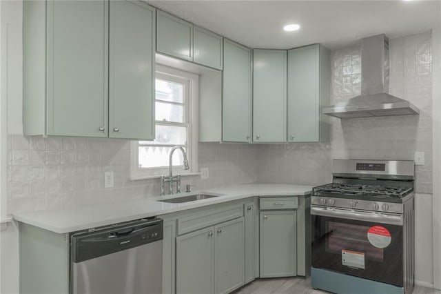 kitchen featuring appliances with stainless steel finishes, wall chimney range hood, light countertops, and a sink