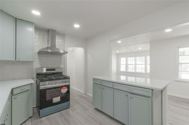 kitchen with stainless steel gas range oven, light wood-style floors, wall chimney range hood, and light countertops