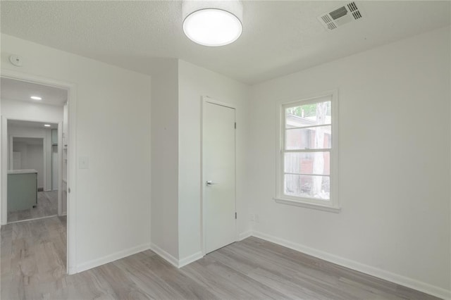 unfurnished bedroom with light wood finished floors, a textured ceiling, visible vents, and baseboards
