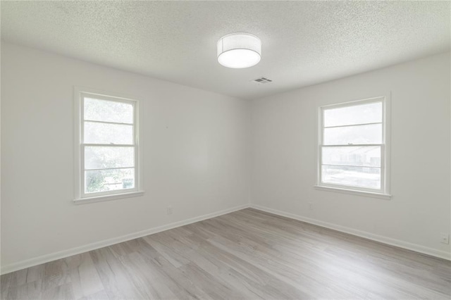 empty room featuring a textured ceiling, visible vents, light wood-style flooring, and baseboards