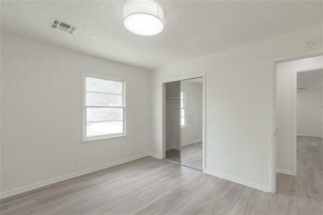 unfurnished bedroom with a closet, light wood-type flooring, visible vents, baseboards, and a textured ceiling