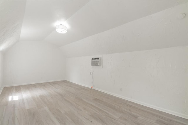 bonus room with a wall mounted air conditioner, baseboards, vaulted ceiling, and light wood-type flooring