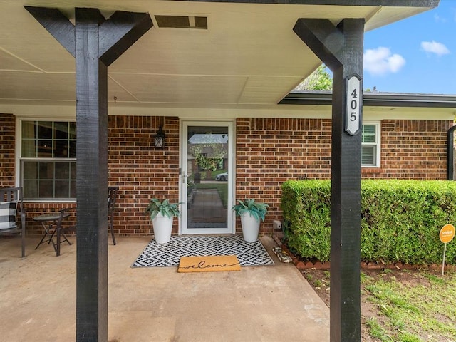 view of exterior entry with brick siding and a patio