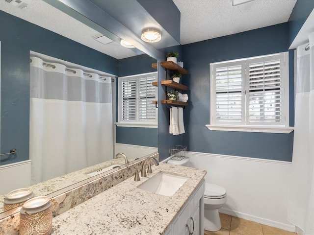 full bathroom featuring tile patterned flooring, vanity, toilet, a textured ceiling, and a wainscoted wall