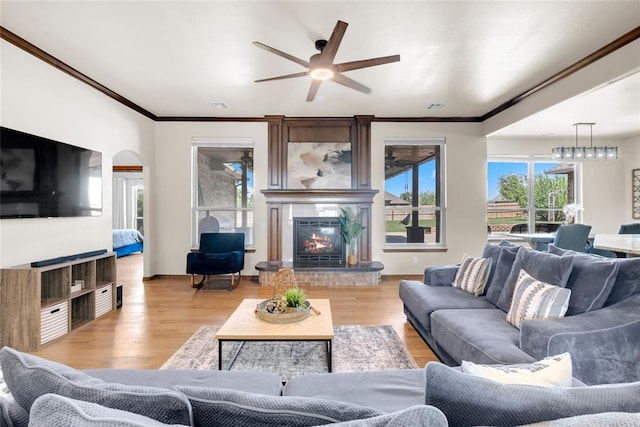 4679 Hillcrest Ln, Edmond, OK 73025 - living room featuring a glass covered fireplace, ornamental molding, a ceiling fan, and light wood-style flooring