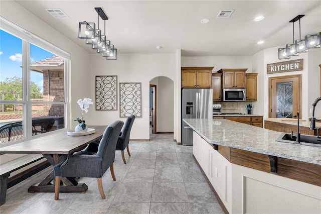 4679 Hillcrest Ln, Edmond, OK 73025 - kitchen with stainless steel appliances, tasteful backsplash, brown cabinets, arched walkways, and light stone counters