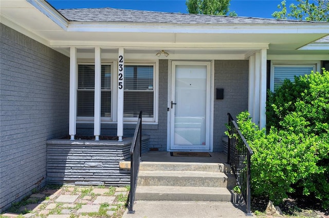 property entrance featuring roof with shingles, a porch, and brick siding