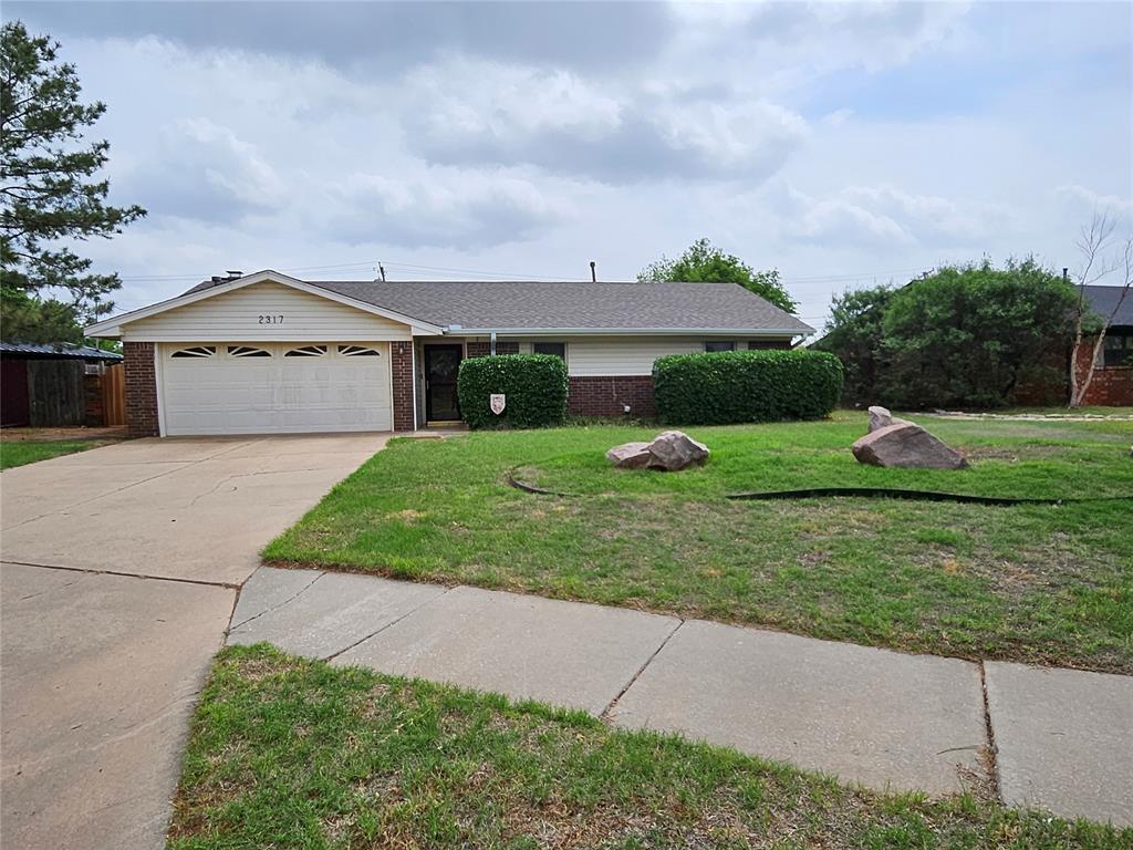 ranch-style home featuring concrete driveway, a garage, a front lawn, and brick siding