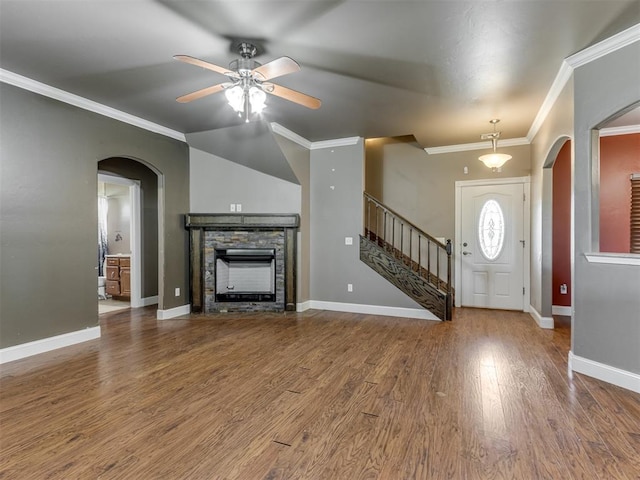unfurnished living room featuring crown molding, ceiling fan, a fireplace, arched walkways, and wood finished floors