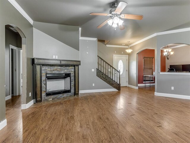 unfurnished living room featuring ceiling fan, a stone fireplace, crown molding, wood finished floors, and stairs