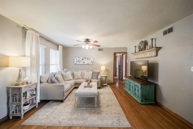 living area with baseboards, visible vents, wood finished floors, and ceiling fan