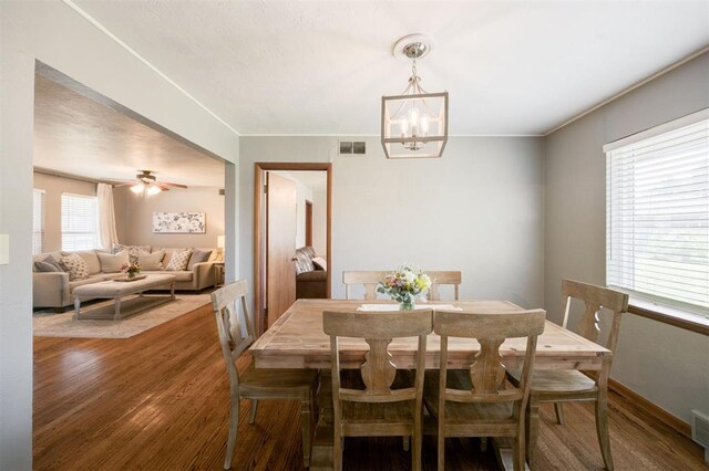 dining space featuring wood finished floors, ceiling fan with notable chandelier, baseboards, visible vents, and crown molding