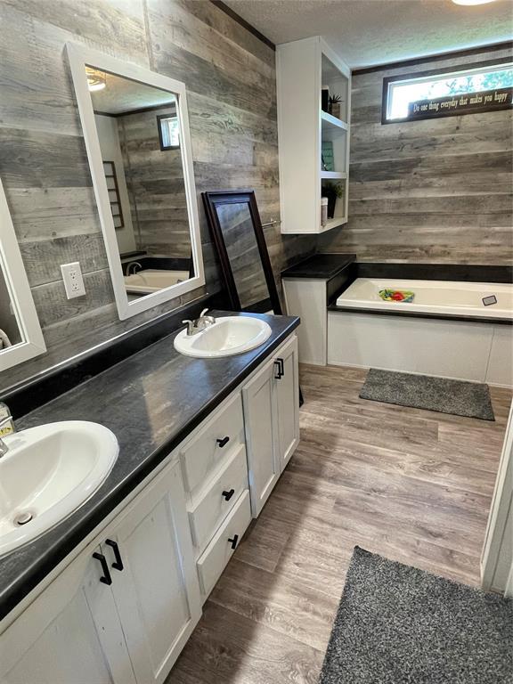 bathroom with a sink, double vanity, wood walls, and a tub to relax in