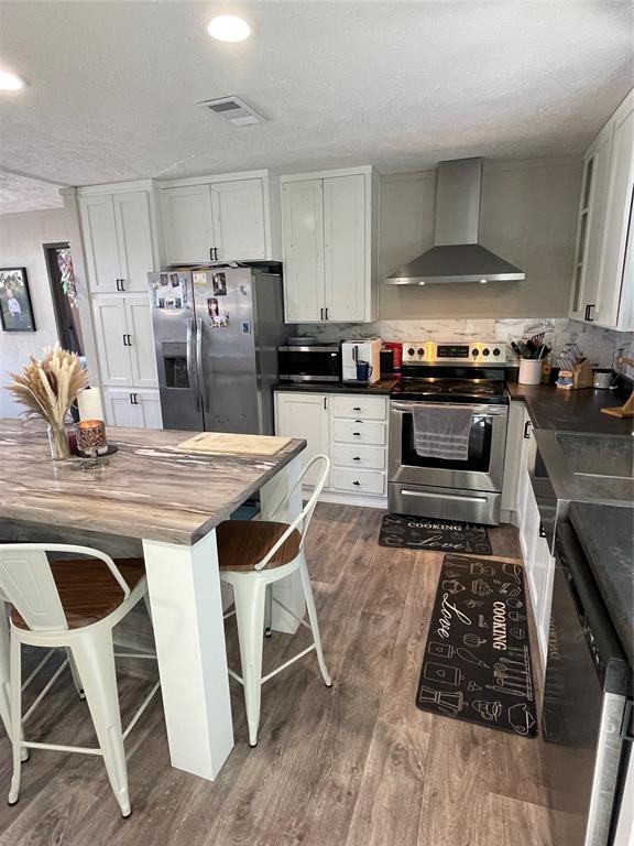kitchen featuring butcher block counters, dark wood-type flooring, wall chimney exhaust hood, tasteful backsplash, and stainless steel appliances