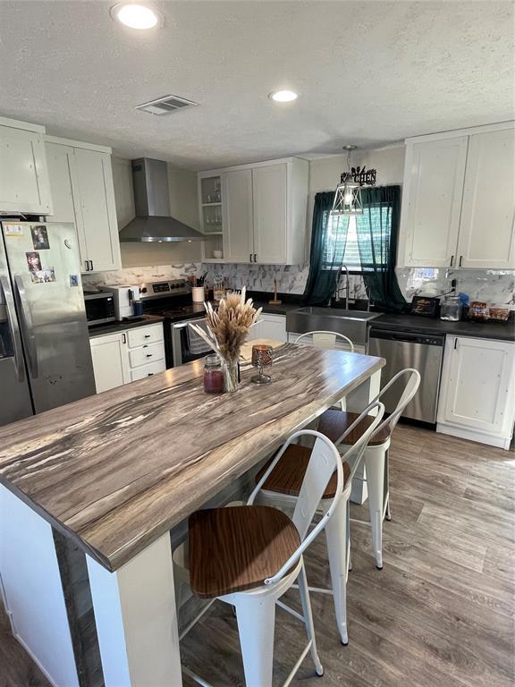 kitchen featuring a sink, wall chimney exhaust hood, stainless steel appliances, backsplash, and visible vents