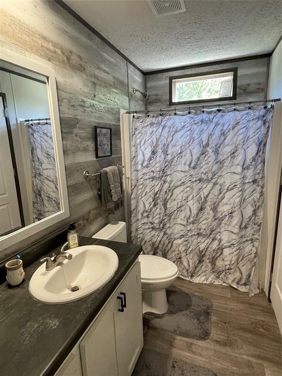bathroom featuring visible vents, wood walls, vanity, wood finished floors, and curtained shower