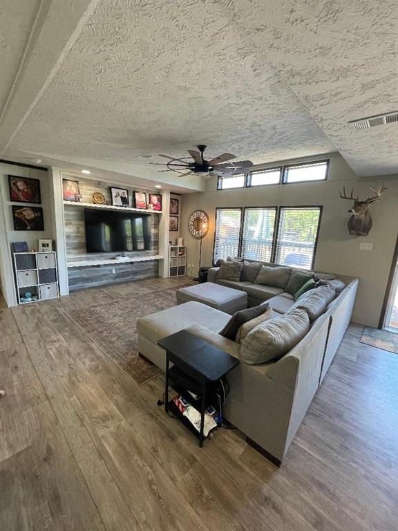 living room with a textured ceiling, ceiling fan, wood finished floors, and visible vents