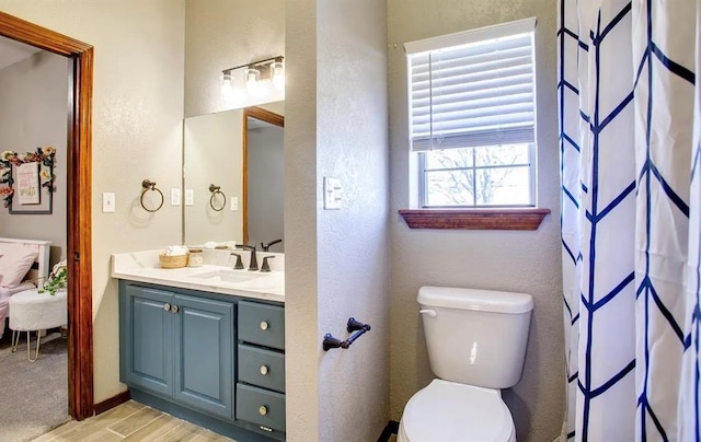full bathroom with wood finished floors, connected bathroom, toilet, a textured wall, and vanity