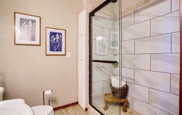 bathroom with baseboards, wood finished floors, a shower stall, and toilet