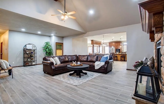 living area with ceiling fan, high vaulted ceiling, a stone fireplace, and baseboards
