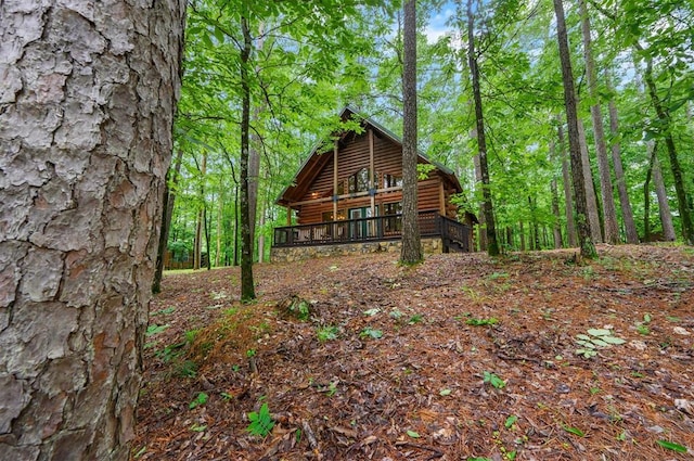 view of side of property with log veneer siding, a deck, and a wooded view