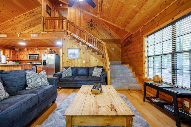 living area featuring vaulted ceiling, wood walls, plenty of natural light, stairway, and light wood-style floors