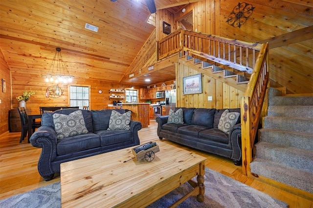 living room featuring stairs, a chandelier, wooden walls, light wood-style floors, and high vaulted ceiling
