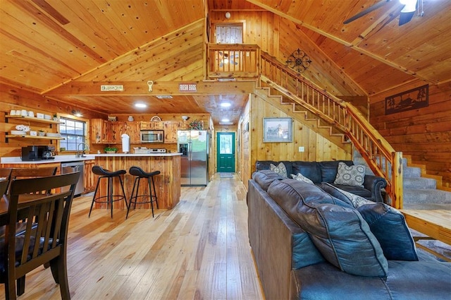 living room featuring wood walls, light wood-style flooring, stairway, lofted ceiling, and wooden ceiling
